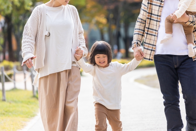 秋の公園で両親に手をひかれる少女の画像
